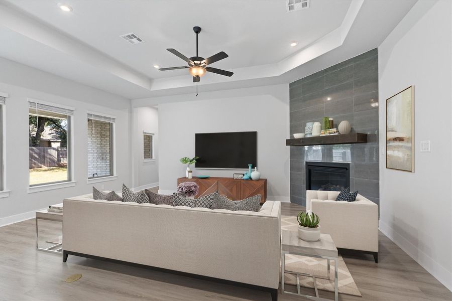 Living room featuring a tiled fireplace, wood finished floors, a tray ceiling, recessed lighting, and ceiling fan