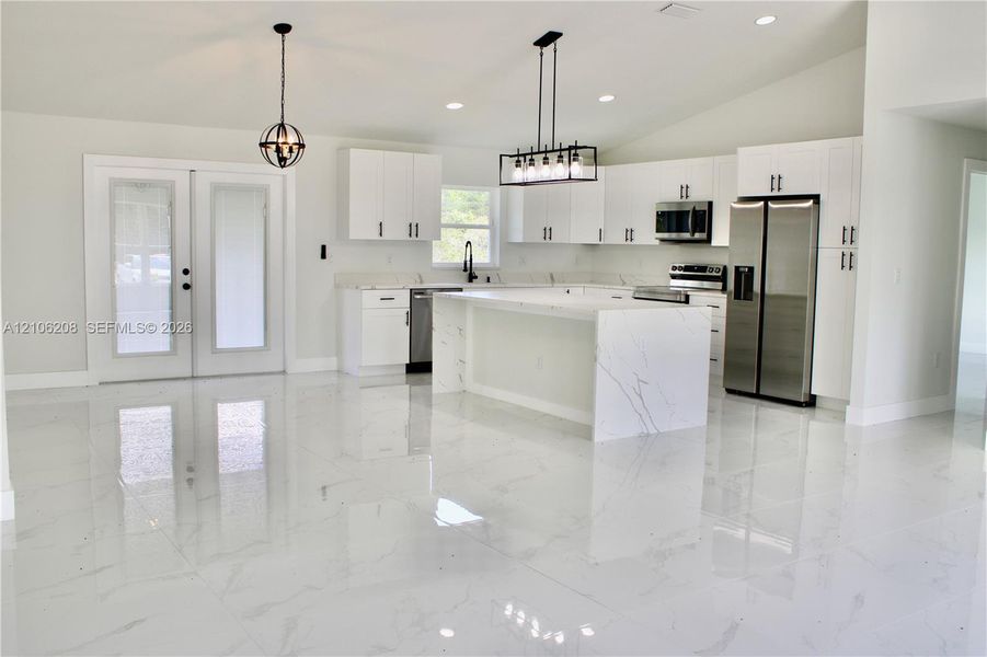 Kitchen featuring white cabinetry, an island with waterfall-edge stone surfacing, stainless steel appliances, and large-format porcelain tile flooring