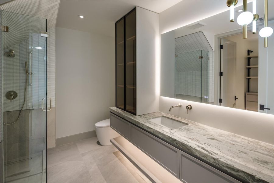 The secondary baths are every bit as considered. A floating vanity, dramatic stone, backlit mirror, glass-front storage, and fully tiled shower bring serious style to this private ensuite.