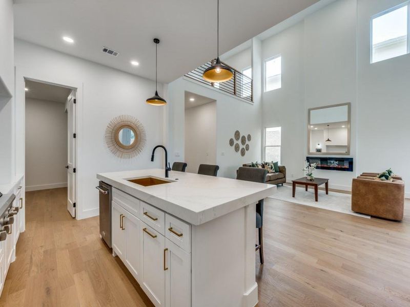 Kitchen featuring a kitchen island with sink, a kitchen breakfast bar, light stone countertops, white cabinetry, and decorative light fixtures