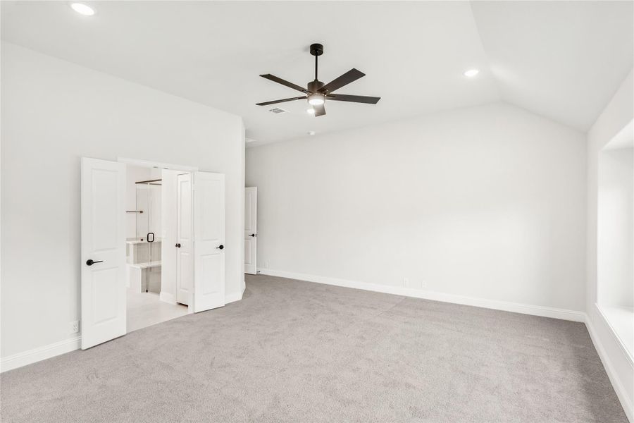 Empty bedroom with vaulted ceiling, ceiling fan, gray carpet, and open walk-in closet doors Empty bedroom with vaulted ceiling, ceiling fan, gray carpet, and open walk-in closet doors