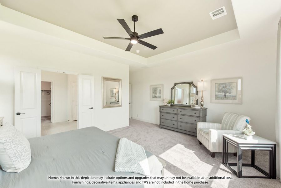 Spacious master bedroom with tray ceiling, ceiling fan, walk-in closet, and neutral carpet flooring