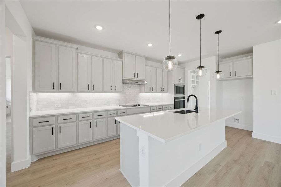 Kitchen featuring backsplash, a kitchen island with sink, decorative light fixtures, white cabinetry, and light wood-type flooring Kitchen featuring backsplash, a kitchen island with sink, decorative light fixtures, white cabinetry, and light wood-type flooring
