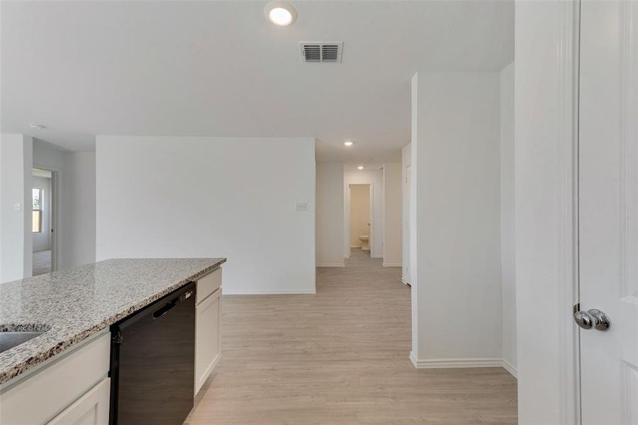 Kitchen with light stone counters, white cabinets, dishwasher, and light hardwood / wood-style floors