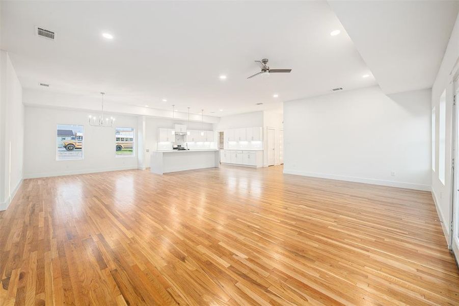 Unfurnished living room with visible vents, light wood finished floors, baseboards, recessed lighting, and ceiling fan with notable chandelier