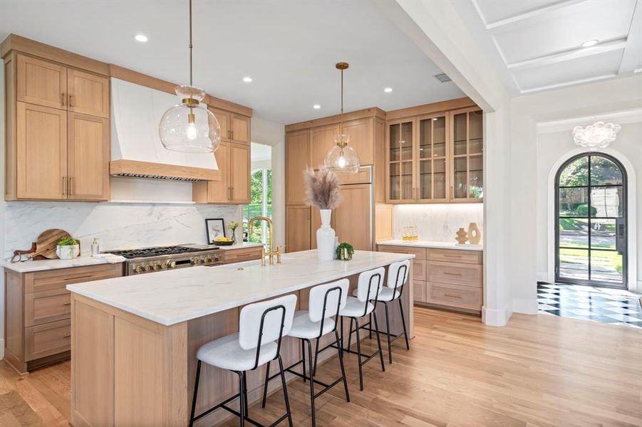 Kitchen with light hardwood / wood-style floors, custom exhaust hood, decorative backsplash, and an island with sink