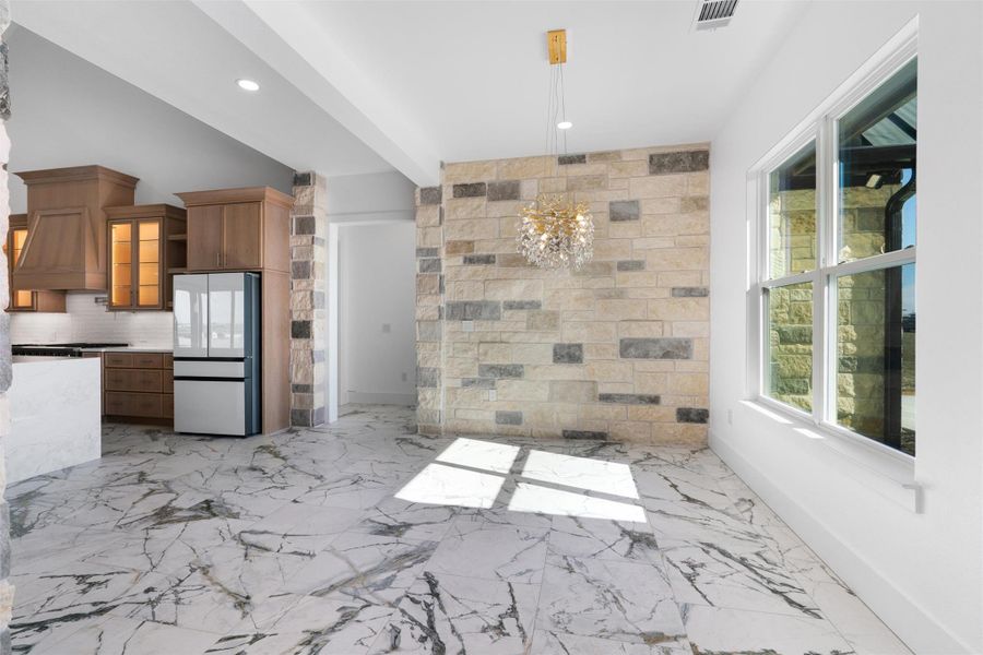 Kitchen featuring freestanding refrigerator, hanging light fixtures, a chandelier, light marble finish flooring, and brown cabinets