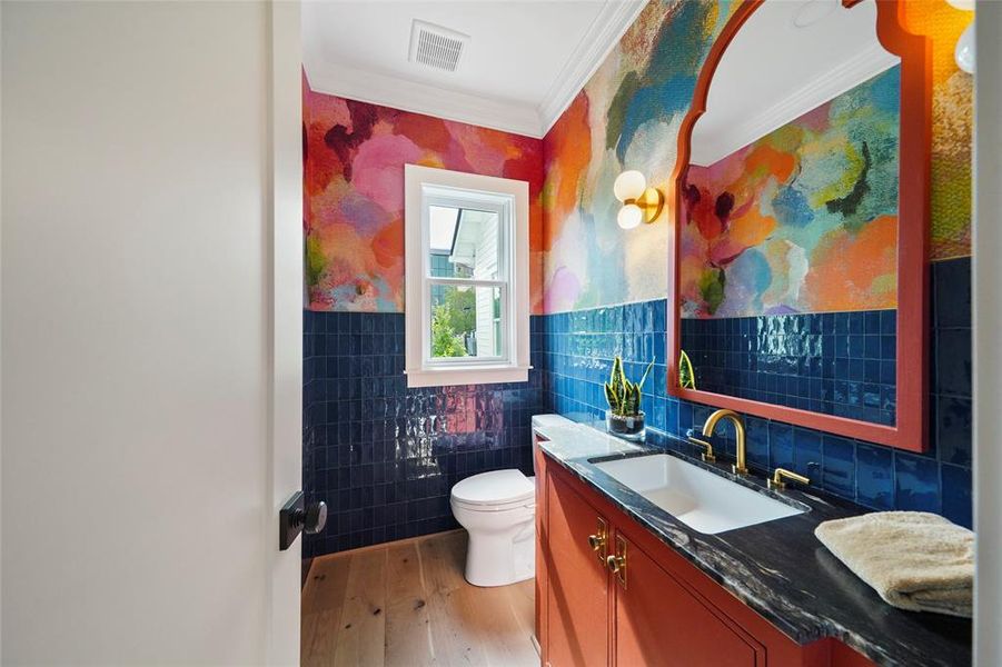 Stunning powder bathroom with vibrant mosaic walls, bold blue tiles, coral vanity, marble countertop, chic gold fixtures, and modern spherical wall sconces.