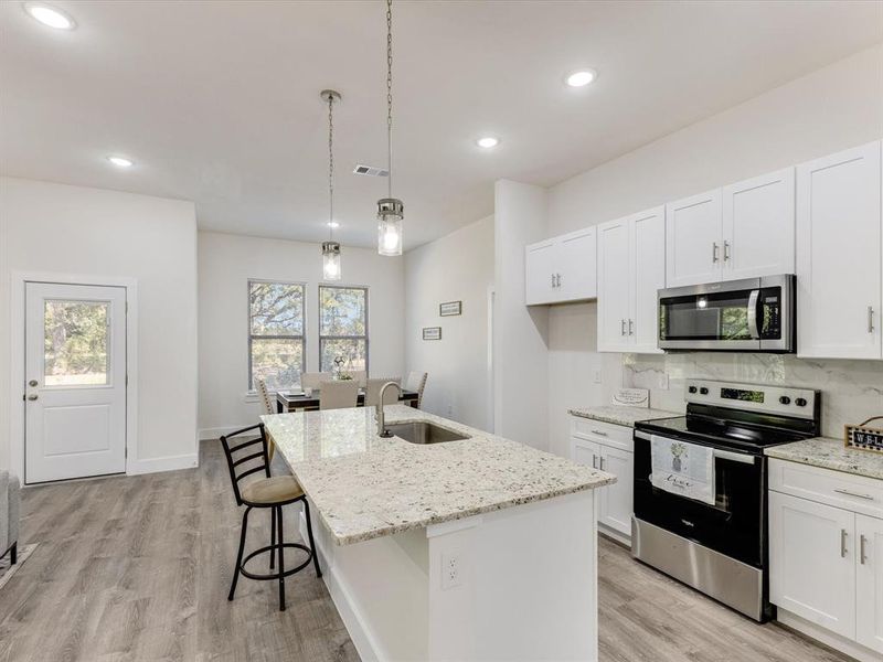 Kitchen featuring stainless steel appliances, a breakfast bar, decorative backsplash, white cabinets, and recessed lighting