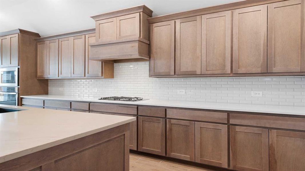 Kitchen featuring appliances with stainless steel finishes, tasteful backsplash, light stone counters, custom exhaust hood, and light wood-type flooring