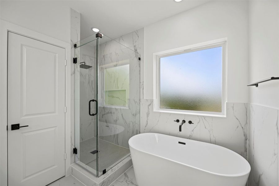 This modern primary bathroom features a sleek freestanding tub, a glass-enclosed shower, and elegant marble-patterned tiles. The large frosted window allows natural light while ensuring privacy.