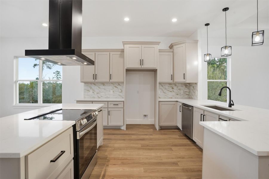 Kitchen with stainless steel appliances, range hood, a peninsula, light stone countertops, and light wood-style flooring