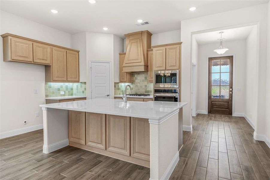 Kitchen with decorative backsplash, light brown cabinetry, light stone countertops, wood tiled floors, and recessed lighting Kitchen with decorative backsplash, light brown cabinetry, light stone countertops, wood tiled floors, and recessed lighting