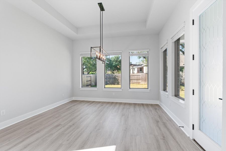 Unfurnished dining area with light wood finished floors, a chandelier, a raised ceiling, and plenty of natural light