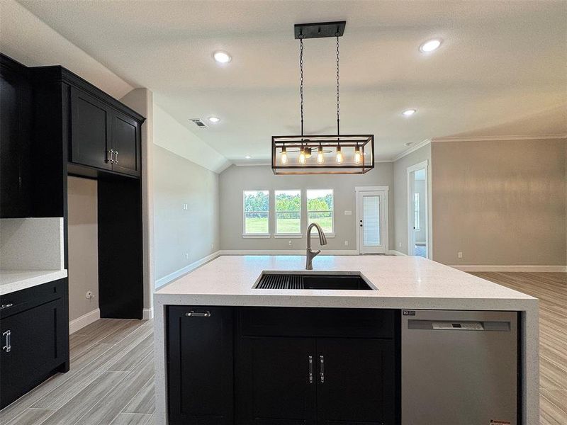 Kitchen island featuring a built-in sink, stainless steel dishwasher, and light-toned countertop
