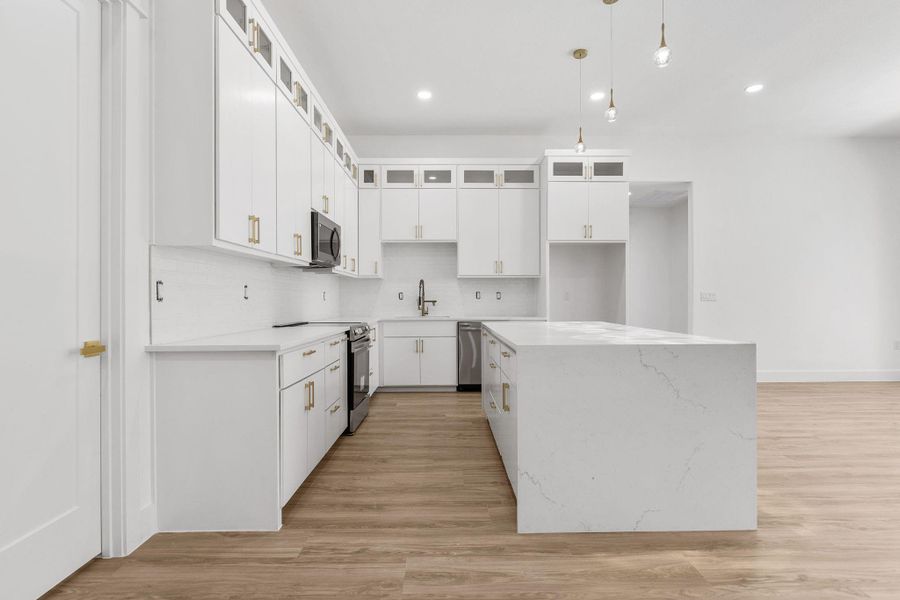 Kitchen with glass insert cabinets, a kitchen island, light wood-style floors, and stainless steel appliances