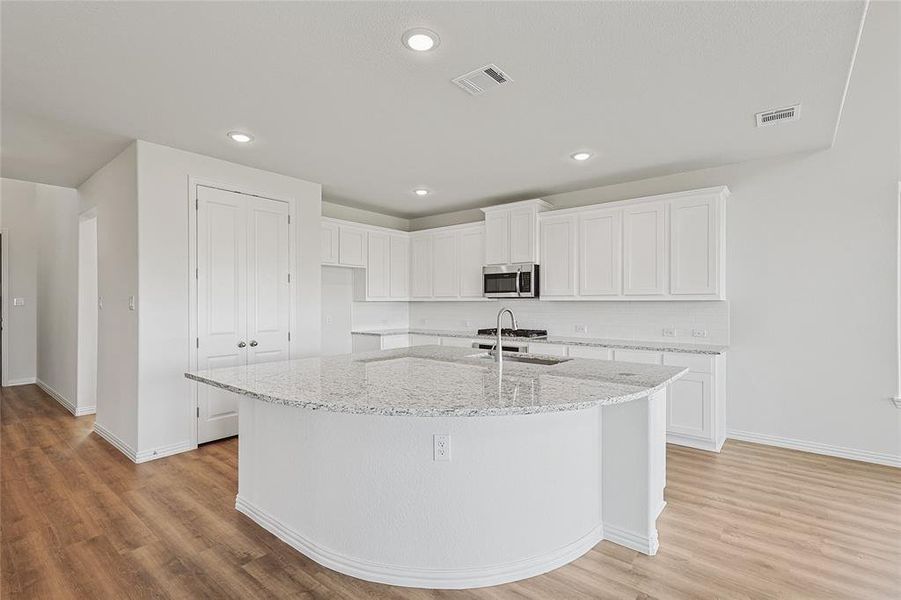 Kitchen featuring an island with sink, light hardwood / wood-style flooring, sink, light stone countertops, and white cabinetry