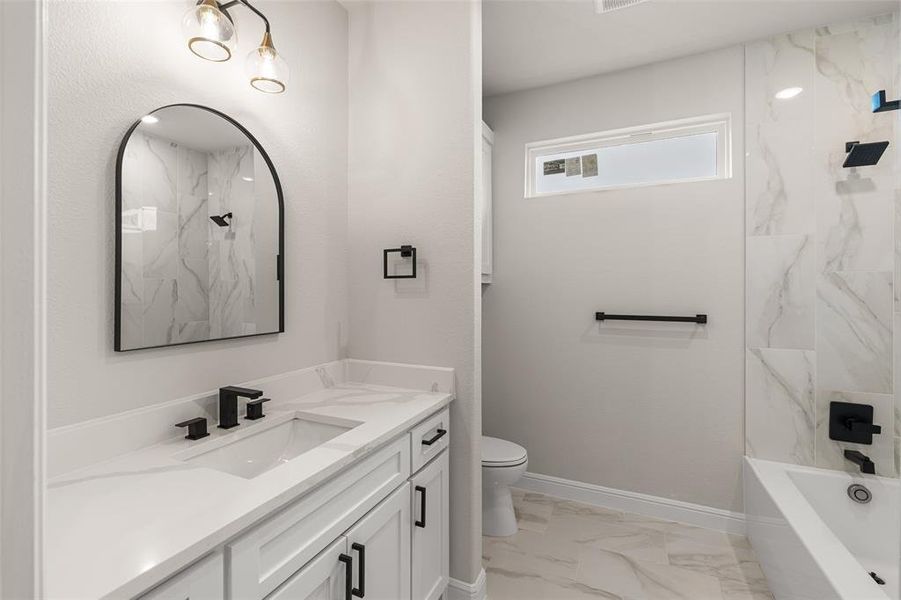 Full bathroom with vanity, tile patterned flooring, tiled shower / bath combo, and toilet