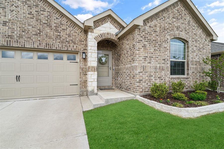 The property showcases a brick exterior with stone accents, a landscaped front yard with a concrete driveway, and a garage with a paneled door