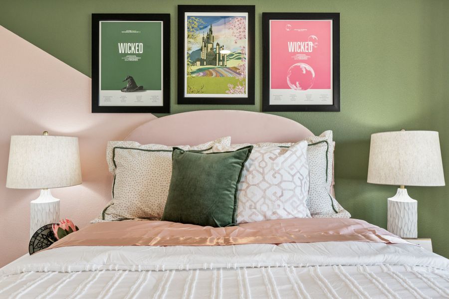Bedroom with pink upholstered headboard, green and pink walls, and three framed Wicked movie posters above the bed
