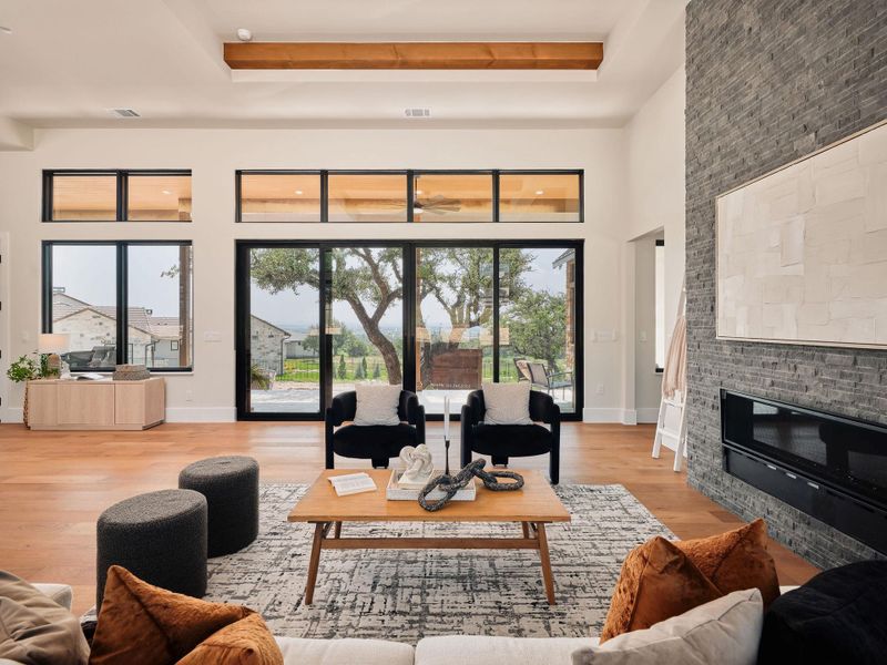 A spacious living area with hardwood floors, a stone fireplace, and ample natural light from large windows. A spacious living area with hardwood floors, a stone fireplace, and ample natural light from large windows.