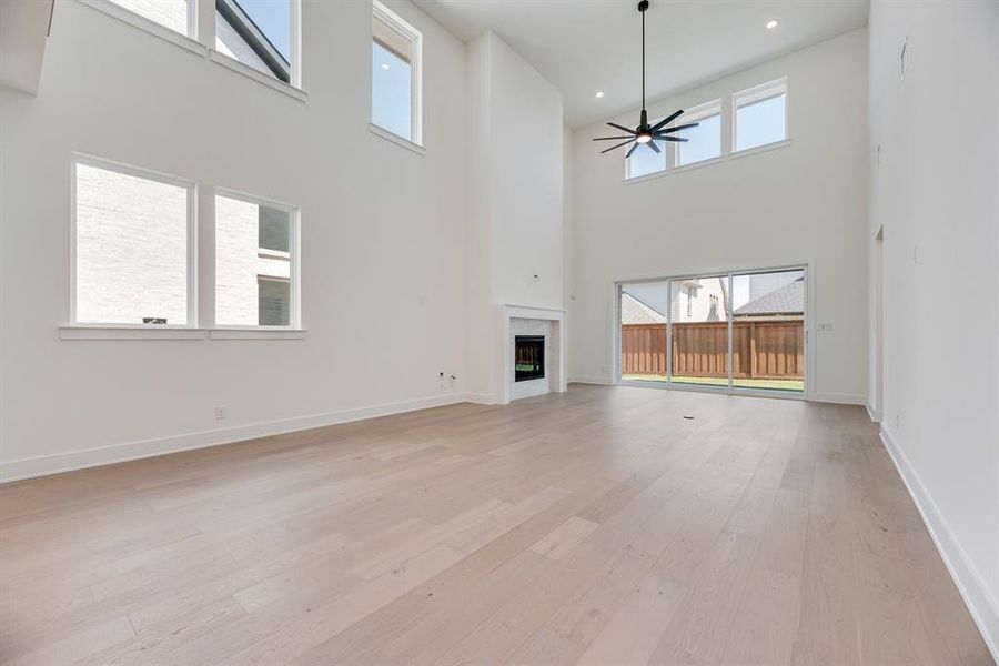 Unfurnished living room featuring a towering ceiling, a glass covered fireplace, light wood finished floors, a ceiling fan, and recessed lighting