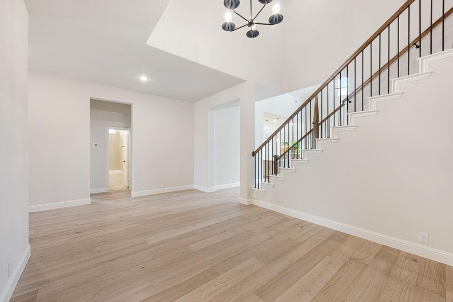 Open living area with light hardwood floors, staircase with iron balusters, and modern chandelier Open living area with light hardwood floors, staircase with iron balusters, and modern chandelier