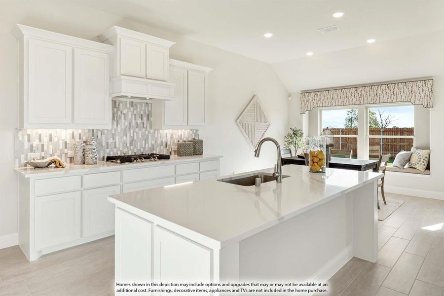 White kitchen with large island, undermount sink, tile backsplash, and breakfast nook with window seat in background.