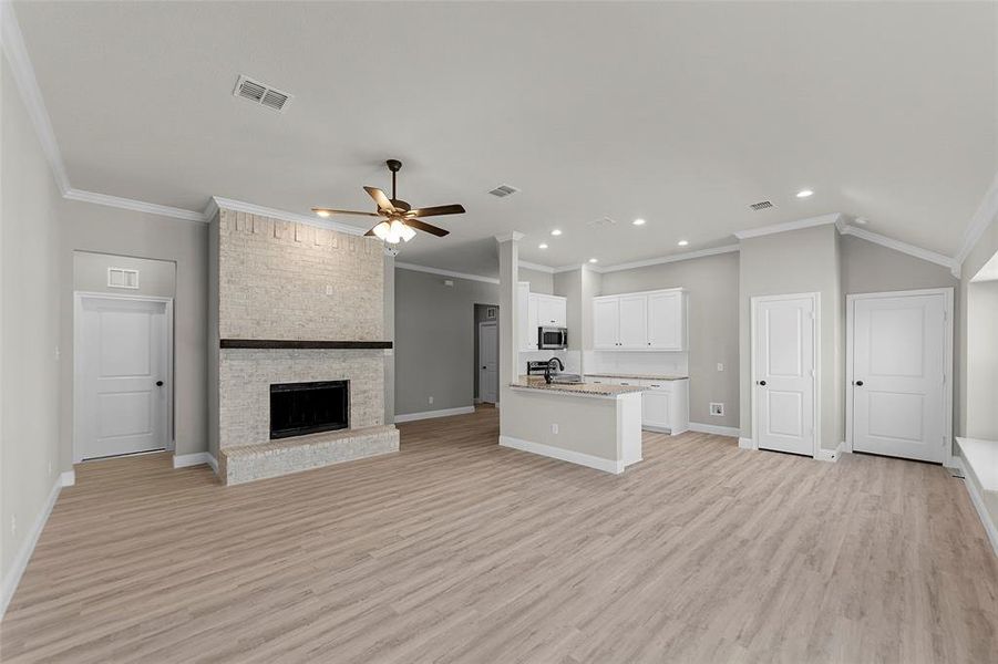 Kitchen featuring open floor plan, white cabinets, an island with sink, light wood-type flooring, and a ceiling fan