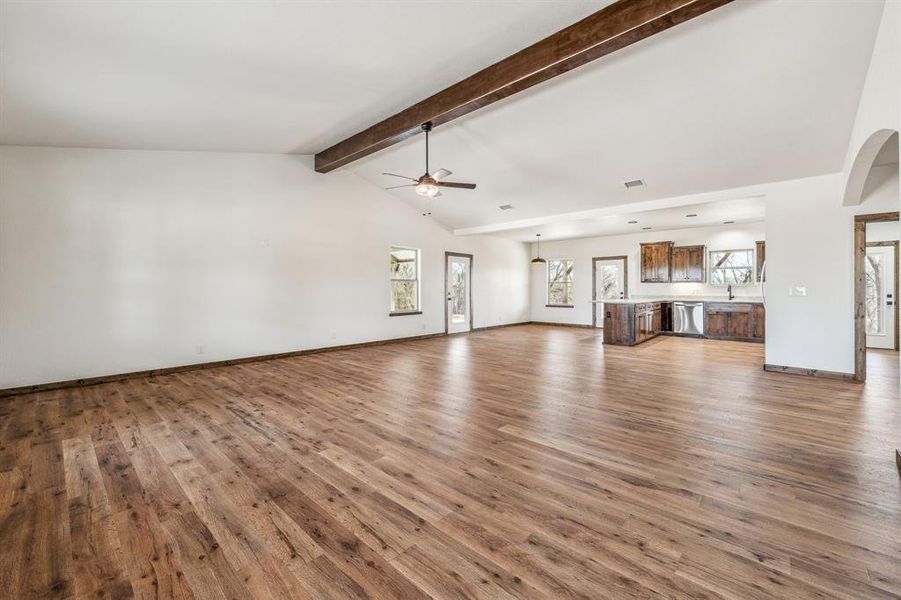 Unfurnished living room with baseboards, beam ceiling, visible vents, a ceiling fan, and wood finished floors