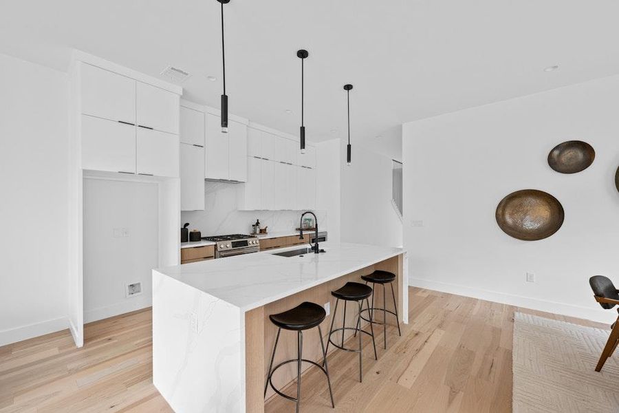 Kitchen featuring white cabinets, modern cabinets, a breakfast bar, light wood-style floors, and stainless steel gas stove