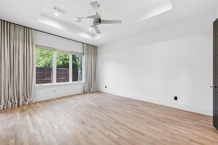 Spare room featuring light hardwood / wood-style floors, ceiling fan, and a tray ceiling