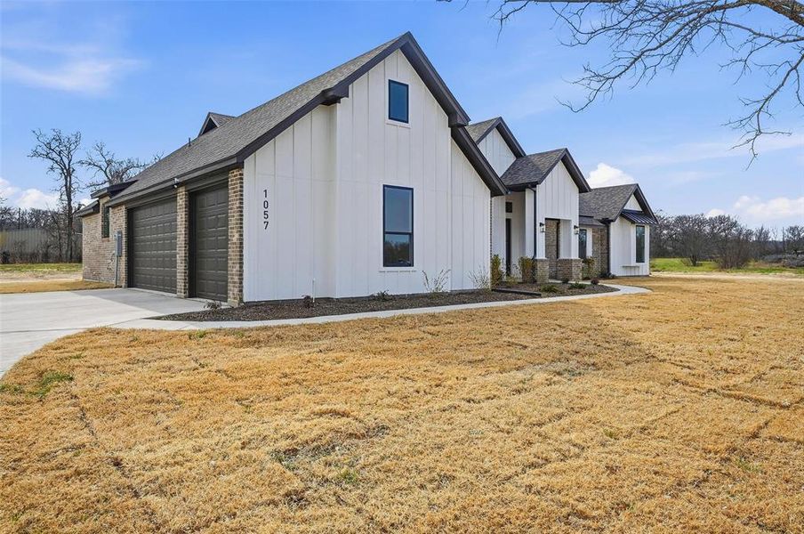 View of side of property featuring board and batten siding, a yard, brick siding, an attached garage, and driveway