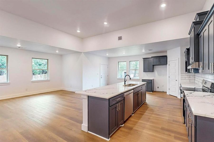 Kitchen featuring stainless steel appliances, a center island with sink, sink, light stone countertops, and light hardwood / wood-style flooring