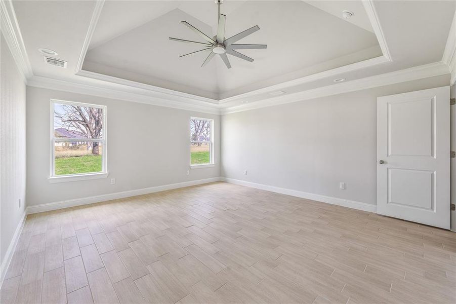 Empty room with a tray ceiling, wood finish floors, ornamental molding, and ceiling fan