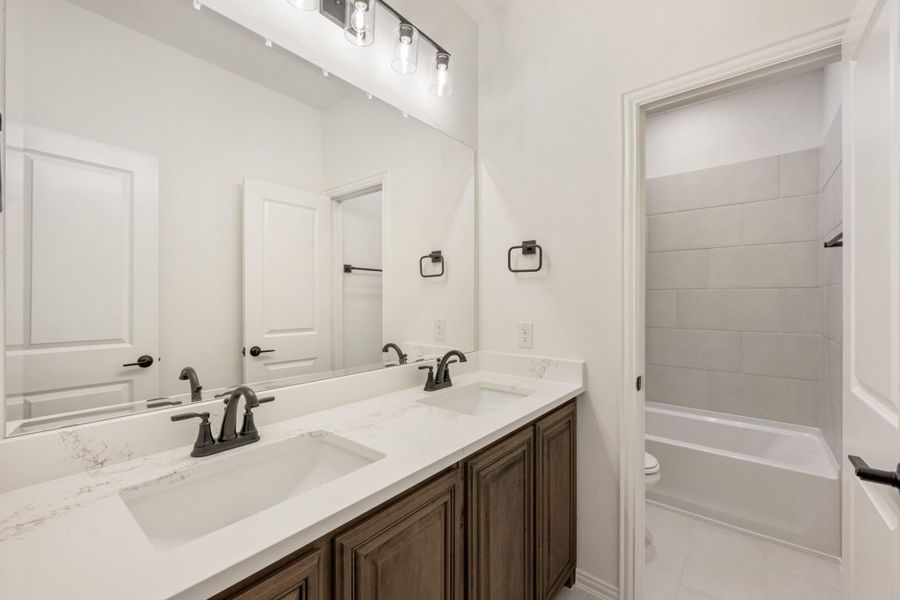 Bathroom with double sink vanity, dark wood cabinets, quartz countertop, and tiled tub-shower combo Bathroom with double sink vanity, dark wood cabinets, quartz countertop, and tiled tub-shower combo