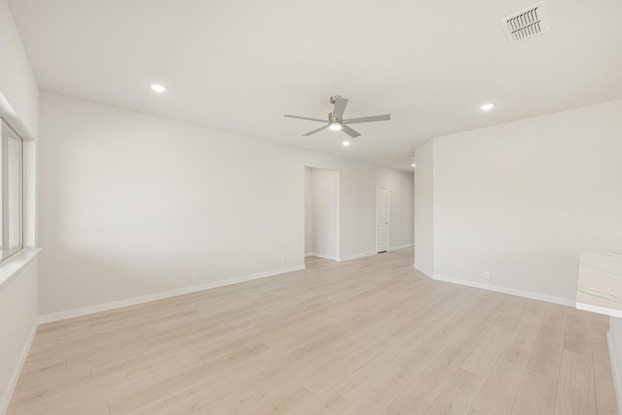 Empty living room with light wood floors, white walls, and ceiling fan with light fixture