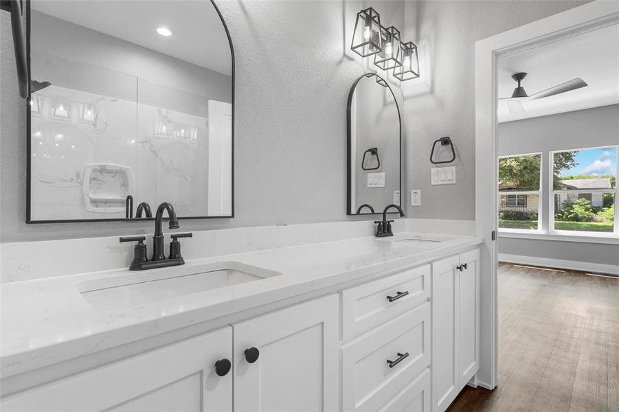 Full bath with double vanity, a marble finish shower, a ceiling fan, and wood finished floors