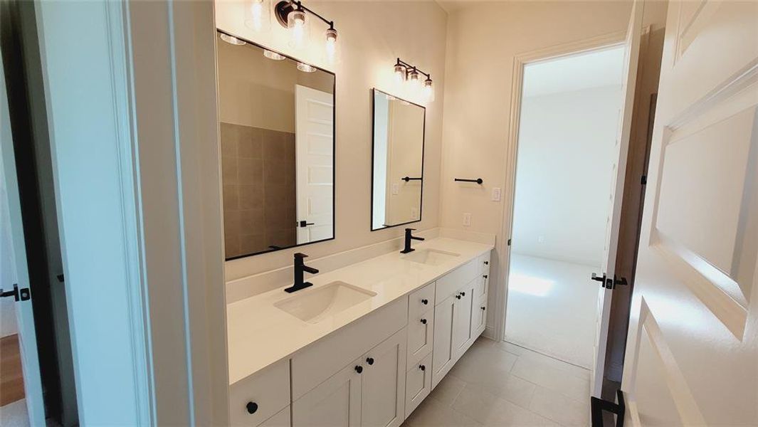 Dual vanity featuring white cabinetry, integrated sinks, black fixtures, and framed mirrors with overhead lighting