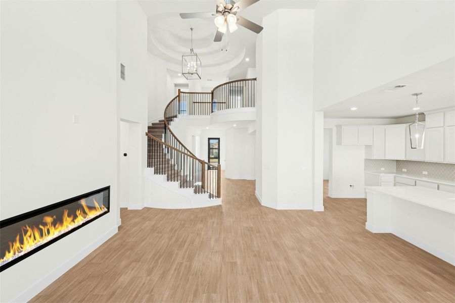 Unfurnished living room with light wood-style floors, a glass covered fireplace, a chandelier, a ceiling fan, and stairs