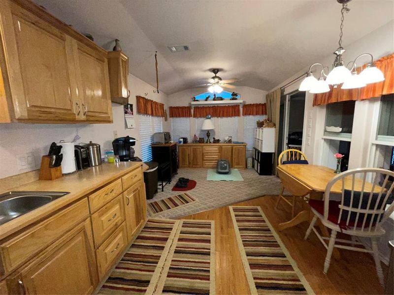 Kitchen with lofted ceiling, hanging light fixtures, hardwood / wood-style flooring, ceiling fan with notable chandelier, and sink Kitchen with lofted ceiling, hanging light fixtures, hardwood / wood-style flooring, ceiling fan with notable chandelier, and sink