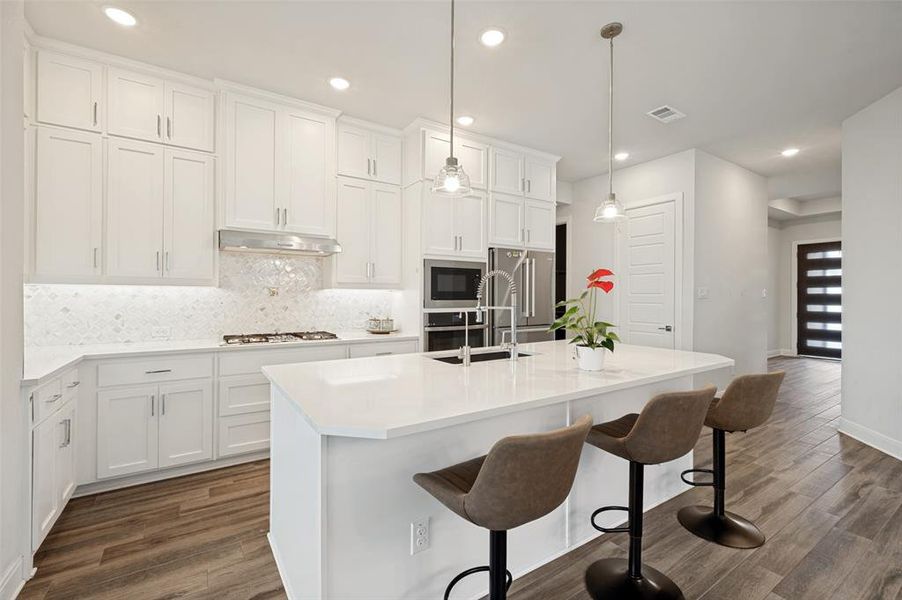 Modern kitchen featuring white cabinetry, a white countertop island with seating, stainless steel appliances, a tile backsplash, and wood-finish flooring