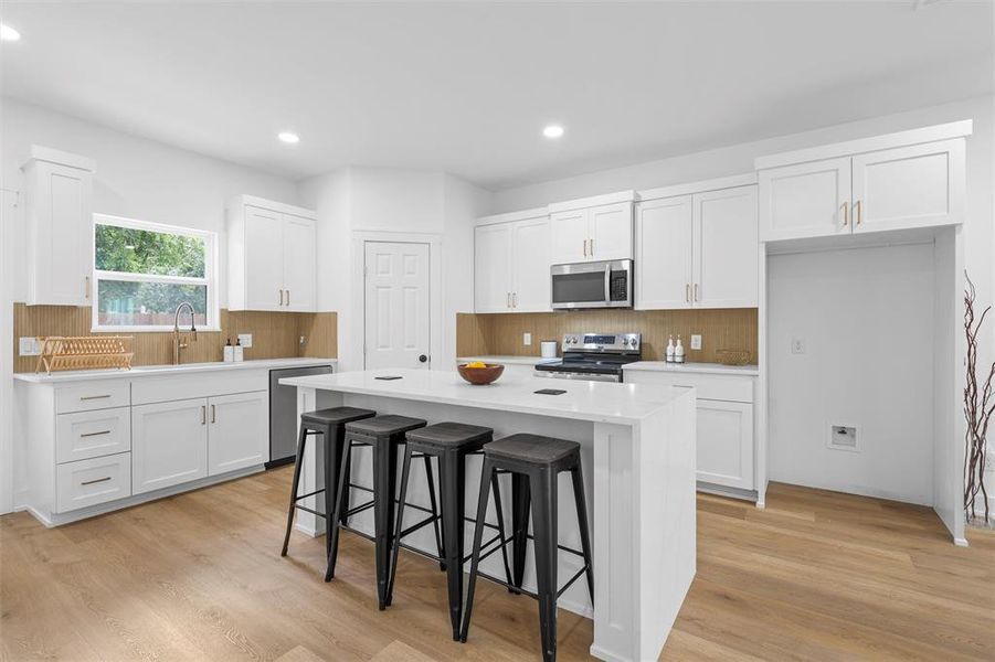 Kitchen featuring stainless steel appliances, backsplash, white cabinets, a kitchen breakfast bar, and recessed lighting Kitchen featuring stainless steel appliances, backsplash, white cabinets, a kitchen breakfast bar, and recessed lighting