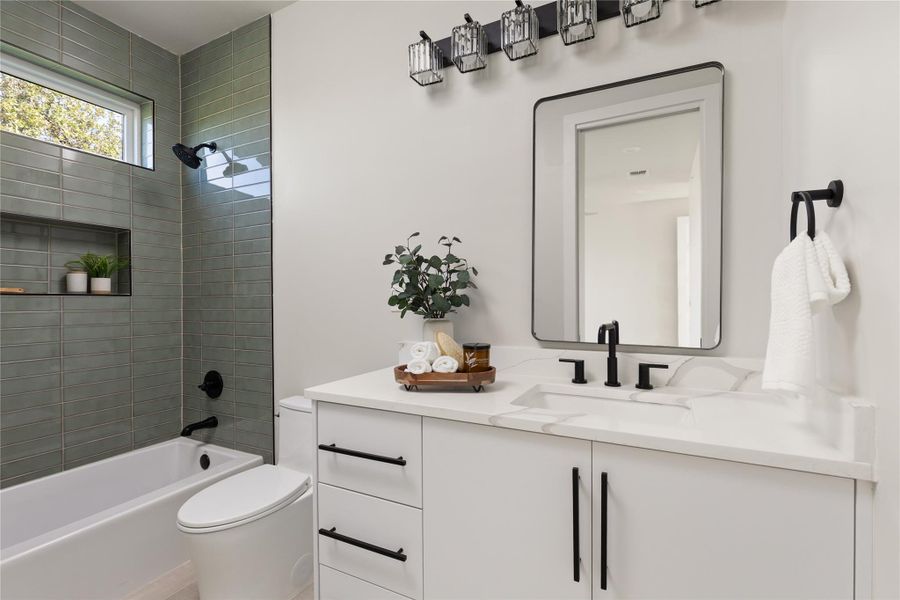 A modern vanity with stone counters complements a tiled tub surround in this updated bathroom.