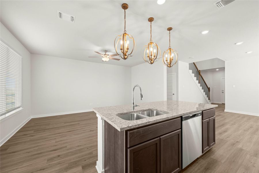 A well-lit kitchen island with granite counters and contemporary light fixtures provides a central gathering point.