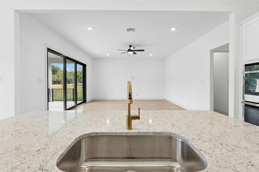 Kitchen featuring light stone counters, recessed lighting, open floor plan, stainless steel double oven, and a ceiling fan Kitchen featuring light stone counters, recessed lighting, open floor plan, stainless steel double oven, and a ceiling fan