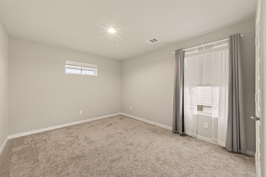 Another secondary bedroom on the second floor features carpeted flooring, a window overlooking the neighboring house, and includes a storage space not shown in the picture.