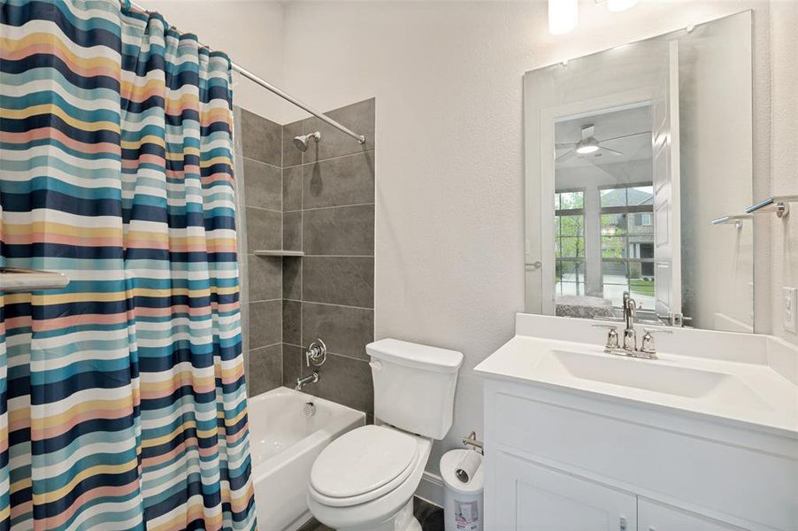 Full bathroom featuring a white vanity with an integrated sink, a white tub, and a shower with gray tile surround and built-in shelving