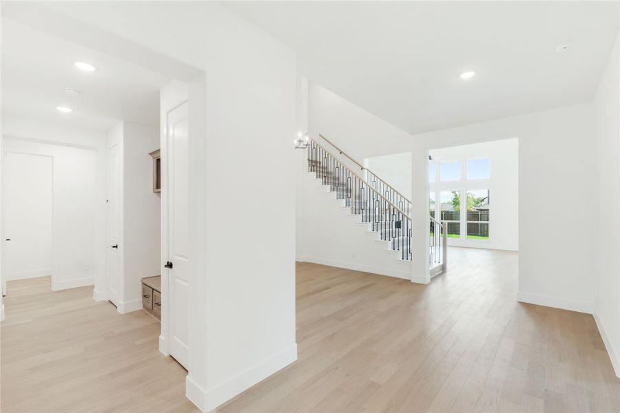 Open home interior with staircase, iron balusters, light hardwood floors, and white walls