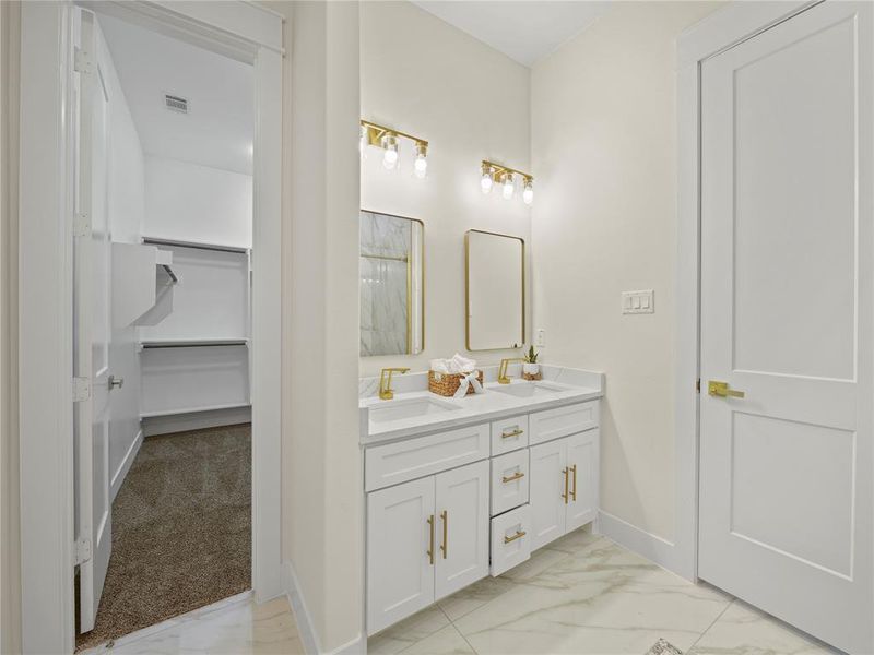 Full bathroom with a walk in closet, double vanity, light marble finish flooring, and light colored carpet
